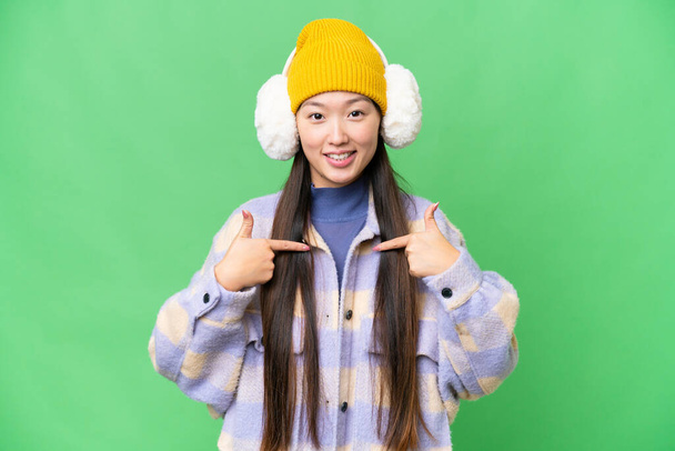 Young Asian woman wearing winter muffs over isolated chroma key background with surprise facial expression - Foto, Bild