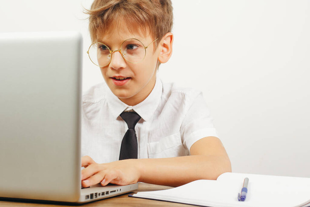 Niño en edad escolar en camisa blanca y corbata interactúa con entusiasmo con el ordenador portátil. - Foto, imagen