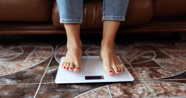Ženské nohy v džínách stojí na elektronických váhách, zblízka. Kontrola stravy. Koncept měření hmotnosti - Záběry, video