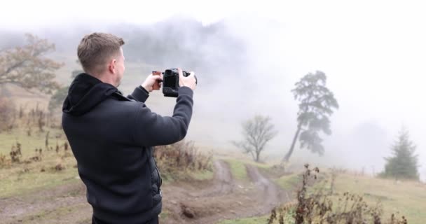 山の上の男は、カメラ、クローズアップの霧の中で森を撮影します。農村道路、秋の風景 - 映像、動画