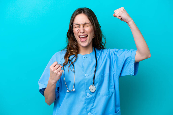 Nuori kirurgi lääkäri nainen eristetty sinisellä taustalla juhlii voittoa - Valokuva, kuva