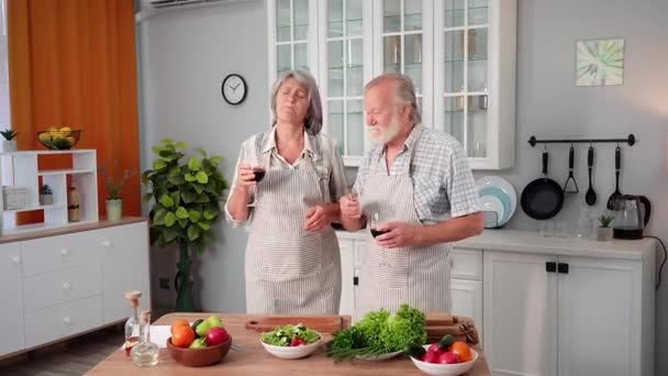 amorosos cónyuges mayores con copas de vino celebrando el aniversario y preparando deliciosa ensalada juntos mientras están de pie en la cocina - Metraje, vídeo