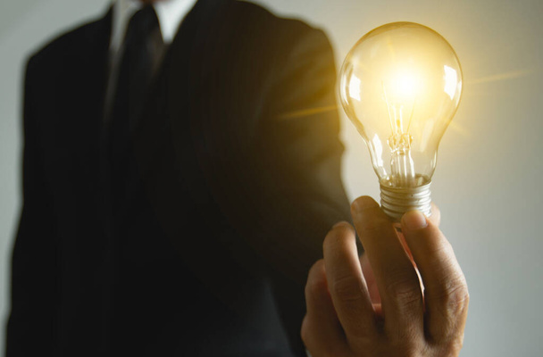 Homme d'affaires tenant une ampoule qui brille de nouvelles idées créatives, innovations Brainstorming, inspiration et idées. Solution homme tenant ampoule de copie de l'espace arrière-plan. - Photo, image
