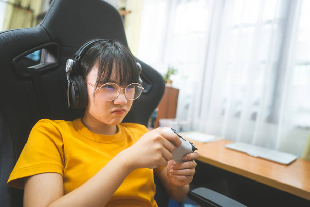 Nerd style young adult asian gamer woman wear eyeglasses play a online game. Competition for victory mood. People leisure lifestyle at home. - Photo, Image