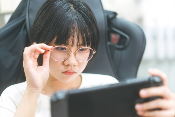 Nerd style jeune adulte asiatique gamer femme porter des lunettes de vue jouer à un jeu en ligne portable. Compétition pour l'humeur de victoire. Loisirs à la maison. - Photo, image