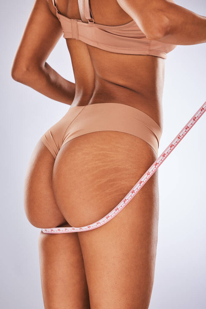 Woman, ass and tape measure in body care, cellulite or weight loss against a gray studio background. Female buttocks measuring size in underwear or lingerie for fitness, diet or healthcare wellness. - Foto, Imagen