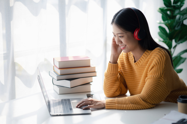 Mujer adolescente asiática sentada en una oficina blanca con computadora portátil, es una estudiante que estudia en línea con computadora portátil en casa, estudiante universitaria que estudia en línea, concepto de educación web en línea. - Foto, imagen