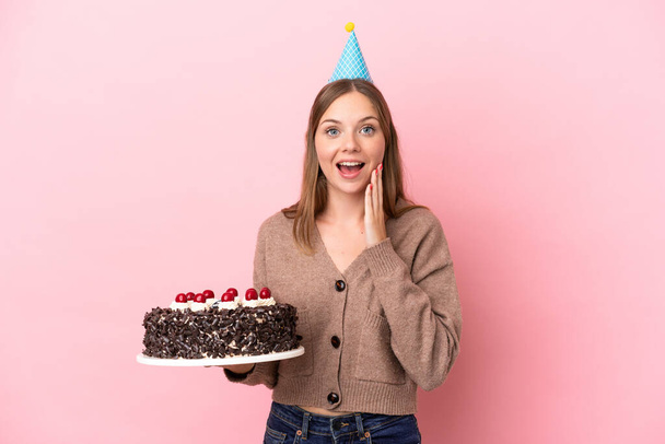 Young Lithuanian woman holding birthday cake isolated on pink background with surprise and shocked facial expression - Fotoğraf, Görsel