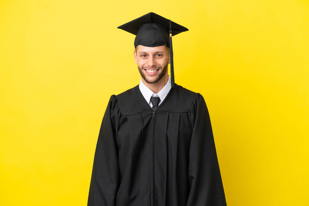 Молодой выпускник университета кавказский человек изолирован на желтом фоне смеясь - Фото, изображение