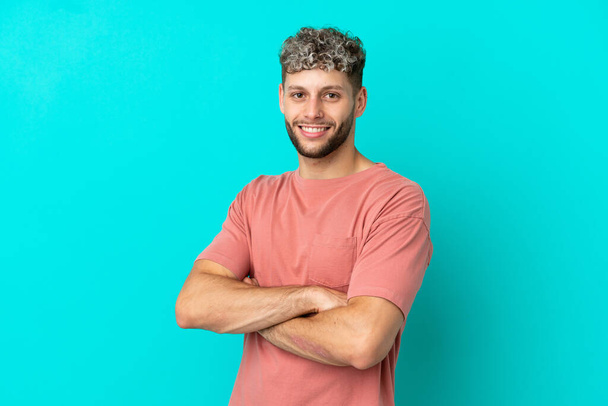 Young handsome caucasian man isolated on blue background with arms crossed and looking forward - Fotó, kép
