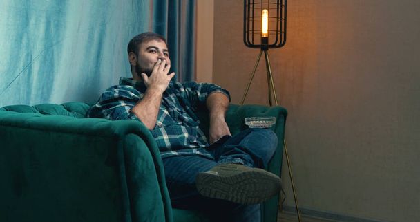 Man smoking cigarette on a green armchair, man checking social media via phone. handsome man smoking a cigarette. Lips blowing smoke. Adult bearded man smoking joint cigarette. - Photo, Image