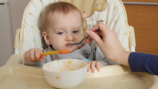 Closeup of mother feeding porridge to her baby son with spoon. Concept of parenting, healthy nutrition and baby feeding - Materiał filmowy, wideo