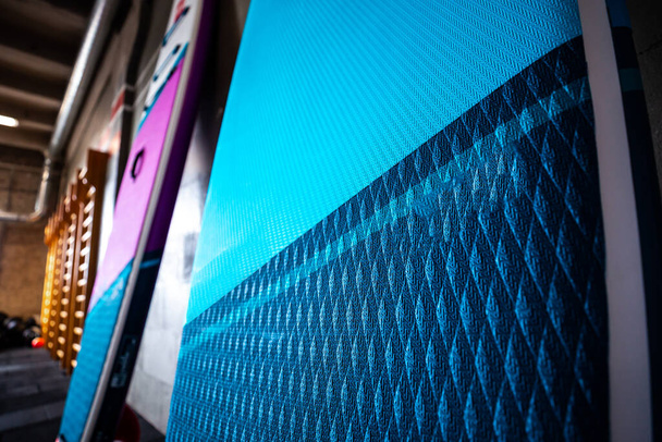 Blaue und pinkfarbene Stand-up-Paddle-Boards SUP an der Wand. Surf- und Surf-Ausrüstung hautnah. - Foto, Bild