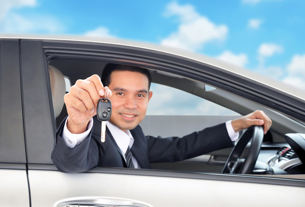 青い空を背景に車のキーを示すドライバーとしてアジア系のビジネスマン - 写真・画像