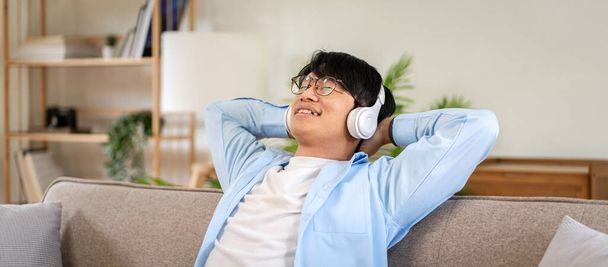 Businessman in casual is sitting on comfortable sofa with hands behind head and wearing headphones to listening the music while relaxation and enjoying with dreamy in living room at home. - Fotoğraf, Görsel