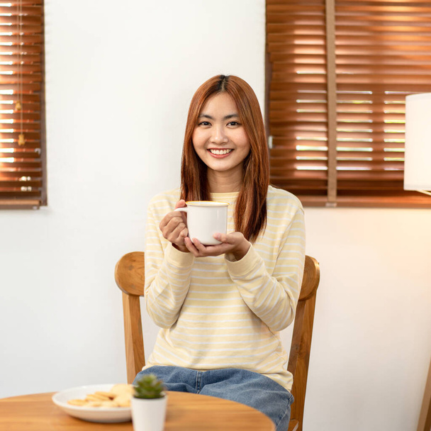 Junge Frau lesbisch blickt Kamera zu lächeln und genießen mit heißer Schokolade trinken, während sie Zeit zur Entspannung im Wohnzimmer zu Hause verbringen. - Foto, Bild