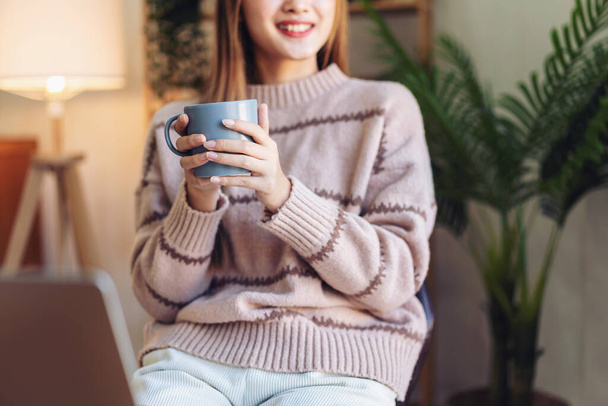 Γυναίκα πίνοντας ζεστή σοκολάτα για να απολαύσετε ονειρικό και χαλαρωτικό με κοιτάζοντας έξω, ενώ κάθεται στην καρέκλα στο σαλόνι για αναψυχή με άνετο τρόπο ζωής στο σαλόνι στο σπίτι. - Φωτογραφία, εικόνα