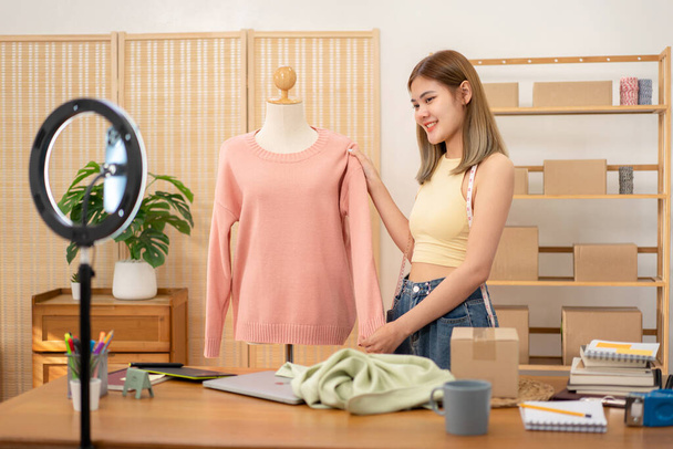 Γυναίκα επιχειρηματίας σχεδιαστής δείχνει πουλόβερ της νέας συλλογής σε μανεκέν και να επανεξετάσει το προϊόν με λεπτομέρεια, ενώ η πώληση του προϊόντος ρούχα σε ζωντανή σύνδεση κοινωνικών μέσων μαζικής ενημέρωσης streaming. - Φωτογραφία, εικόνα