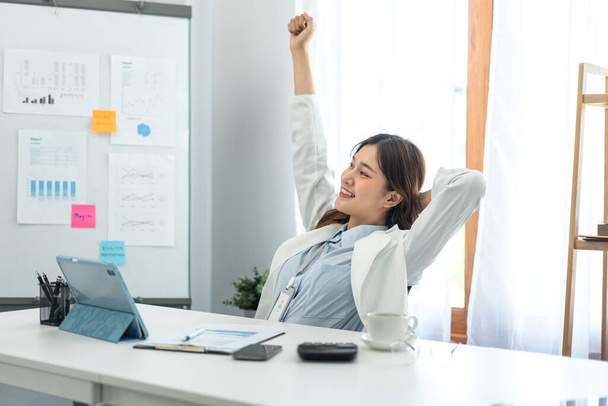 Businesswoman in suit is clenching fists raise up and smile to stretching while working to thinking and analysis about strategy and planning of new business in modern office. - 写真・画像