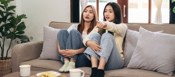 Young woman lesbian couple watching horror movie and pointing with excited face while spending time to relaxation together on big comfortable sofa at home. - Фото, зображення