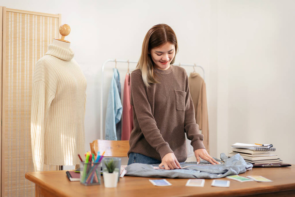 Vrouw ontwerper ondernemer met behulp van meetlint te meten borst grootte van shirt en het controleren van detail tijdens het werken met design nieuwe collectie in huis workshop. - Foto, afbeelding
