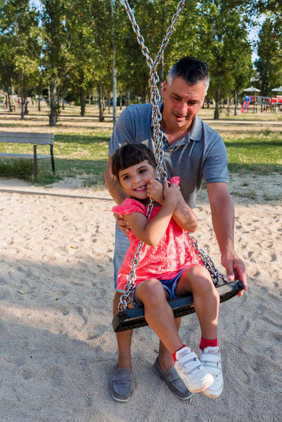Father and daughter having fun playing with the swing in a park. Family concept. - Zdjęcie, obraz