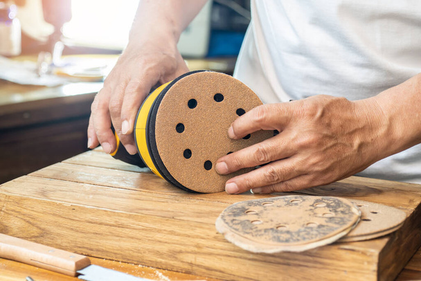 Carpenter attach sandpaper to an orbital sander or palm sander after remove the paper backing of the sandpaper.DIY maker and woodworking concept. selective focus - Photo, image
