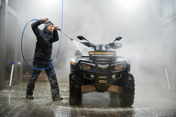 Full length of man washing all-terrain vehicle with high pressure water sprayer auto washer - Foto, Imagen