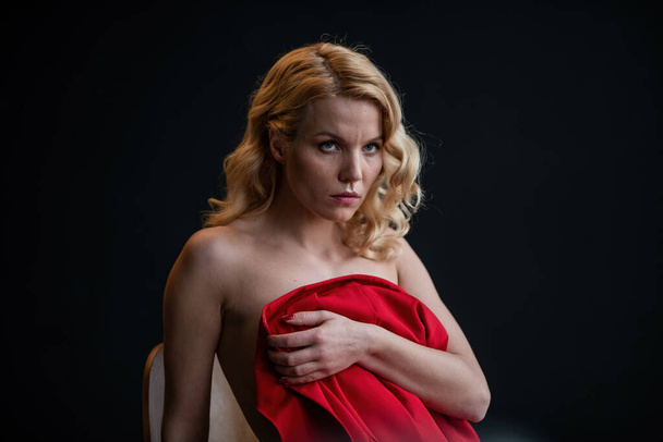 Adult beauty woman bare back in formal evening red trousers sitting pose without bra. Stylish blonde curly hair sensual nude model fashionista posing at studio in fashion pantsuit out of blazer - 写真・画像