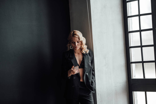 Adult beauty woman in formal evening suit of black color with lace bra taking photo for social media. Stylish blonde curly hair model fashionista posing in fashion pantsuit no shirt video calling - Fotografie, Obrázek