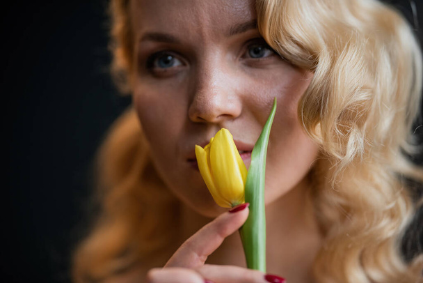 Adult beauty woman half naked in formal evening red trousers without bra hugs bouquet of yellow tulips. Stylish blonde curly hair sensual nude model fashionista posing in studio at spring holidays - Fotó, kép