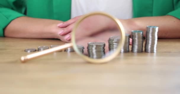 Magnifying glass lying in front of piles of coins in ascending order and businesswoman closeup 4k movie slow motion. Increasing business profits concept - Séquence, vidéo
