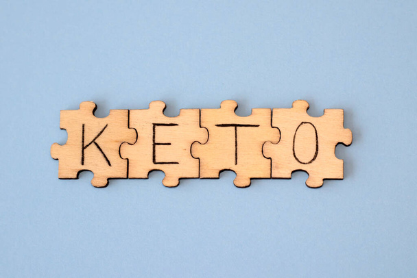 The word Keto made of wooden puzzles on a blue background. Flat view from above - Zdjęcie, obraz