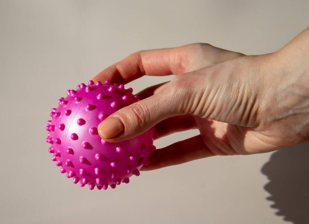Μια γυναίκα κρατάει μια ροζ μπάλα με καρφιά. Μπάλα μασάζ μπορεί να σας βοηθήσει να απελευθερώσετε πόμολα και πόνο. Οφέλη από τη χρήση ενός μπάλα μασάζ για Myofascial Release. - Φωτογραφία, εικόνα