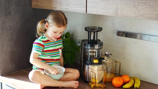 Little girl making fresh juice sitting on the table in home kitchen. High quality 4k footage - Imágenes, Vídeo