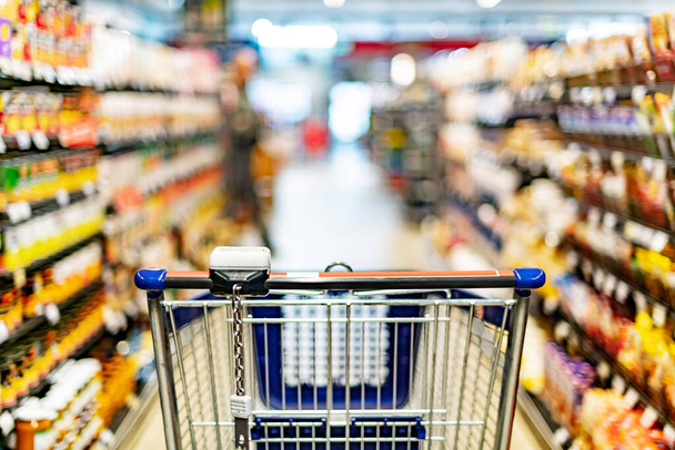 Un carrito de compras junto a un estante de una tienda en un supermercado - Foto, imagen