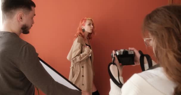 Modelo pelirroja femenina actuando durante una sesión de fotos en estudio con fotógrafo y asistente - Metraje, vídeo