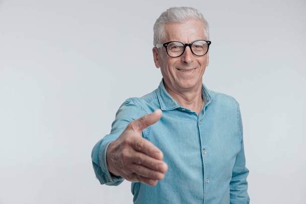 vieil homme dans la soixantaine avec des lunettes serrant le geste de la main et se présentant devant fond blanc - Photo, image