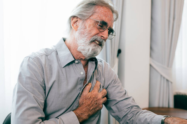 Senior man holding hand on chest and suffering from heart problem at home, Grandfather with heart attack suffer, People with health problems - 写真・画像
