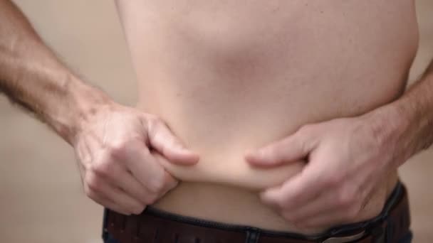 El hombre sostiene pliegues de grasa en su estómago con sus manos, se vuelve hacia diferentes lados.  - Metraje, vídeo