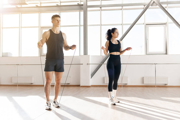 young athletic couple in training jump rope in the gym in the morning, man coach and woman go in for sports, healthy lifestyle - Photo, Image