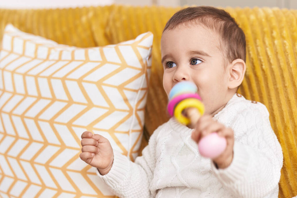 Adorable hispanic toddler sucking toy sitting on sofa at home - Foto, immagini