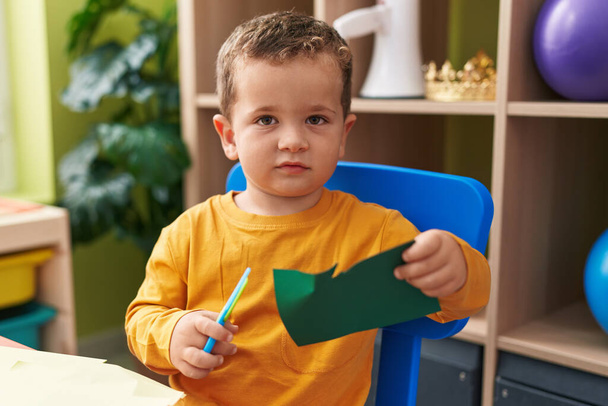 Uroczy biały chłopiec student cięcia papieru siedzi na stole w przedszkolu - Zdjęcie, obraz