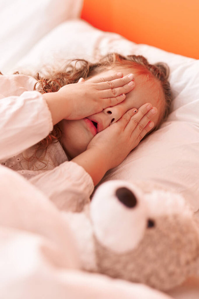 Очаровательный блондинка ребенок подчеркнул, лежа на кровати покрывая глаза руками в спальне - Фото, изображение
