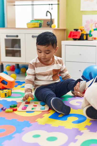Uroczy latynoski maluch gra logiczna matematyki siedzi na podłodze w przedszkolu - Zdjęcie, obraz
