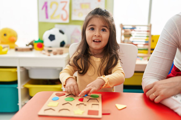 Adorable hispanic girl playing with maths puzzle game sitting on table at kindergarten - Photo, Image