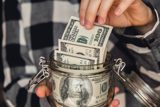 Dollar banknote saving money in glass jar. Unrecognizable woman moderate consumption and economy Collecting money. Tips. Business, finance, saving, banking and people concept. Extra money, passive income. Saving for travel, crisis, house, car, educat - Foto, immagini