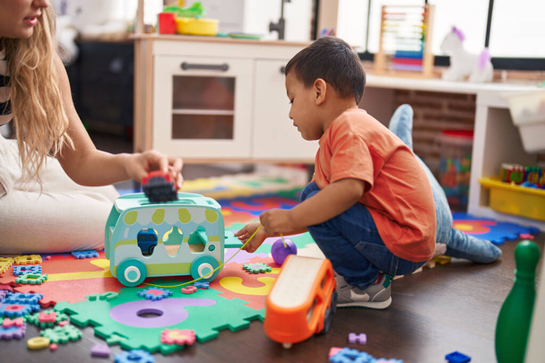Вчитель і малюк грають з машинами іграшка сидить на підлозі в дитячому саду
 - Фото, зображення