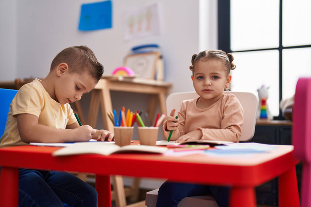 Двоє дітей дошкільного віку сидять на столі, малюючи на папері в дитячому садку
 - Фото, зображення
