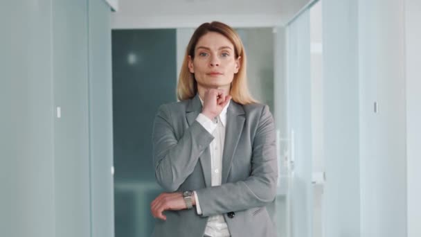 Middle aged confident focused business woman in formal suit standing in modern light office puts hand on chin smile looks at camera feels happy. 40s pretty positive female face portrait concept - Materiaali, video